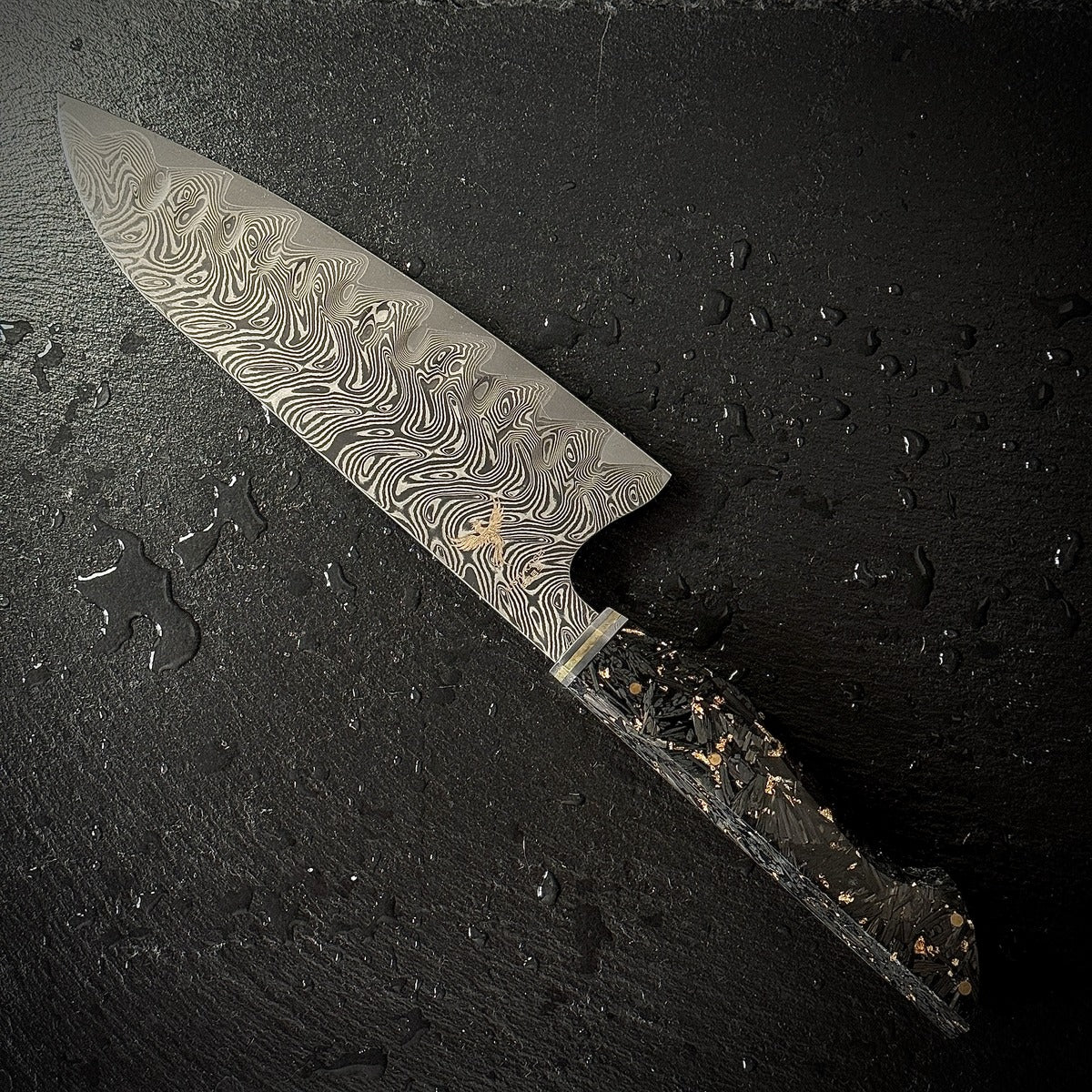 Couteau Santoku japonais, lame en acier damassé AUS-10, manche en carbone et feuilles d'or, posé sur ardoise